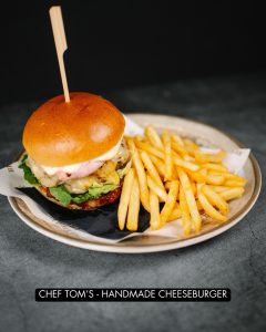 Cheeseburger on a plate in front of a backdroup with fries.