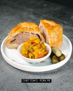 Homemade pork pie on a plate with picallili.