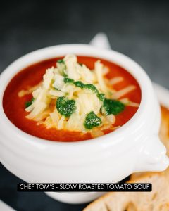 Slow roasted tomato soup in a bowl topped with gruyere crutons, cheese and pesto.