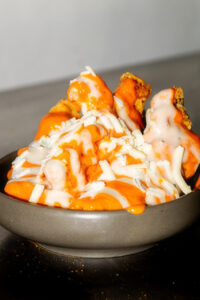 Bowl of fried food topped with orange sauce and white cheese or crema, melting over the pieces.
