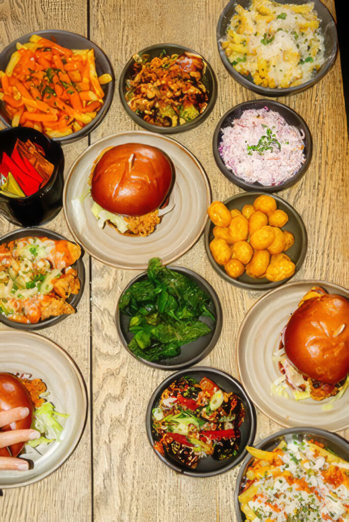 Assorted bowls of food on a wooden table, including burgers, vegetables, and grains, ready for sharing