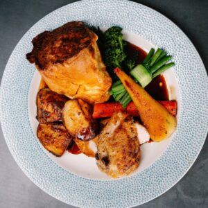 Roasted chicken with potatoes, carrots, green beans, broccoli, and gravy on a blue-patterned plate.